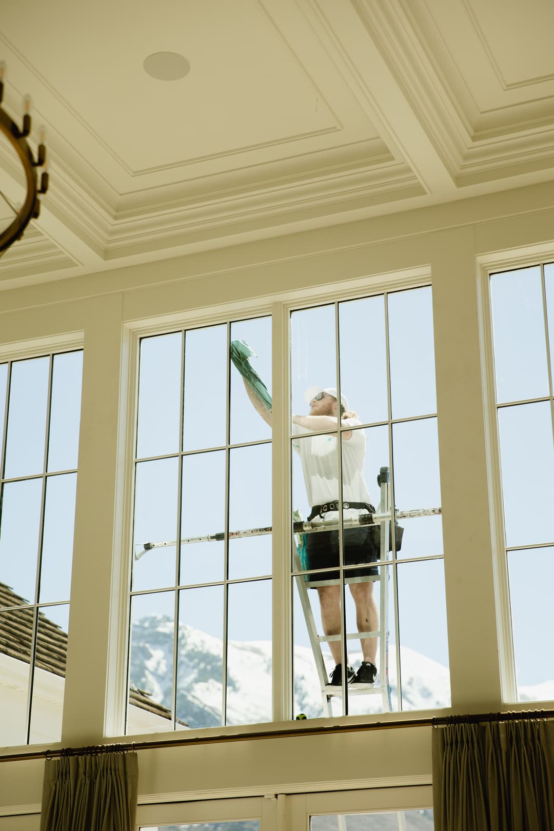 Window cleaner on a ladder washing large windows with mountain view in the background.
