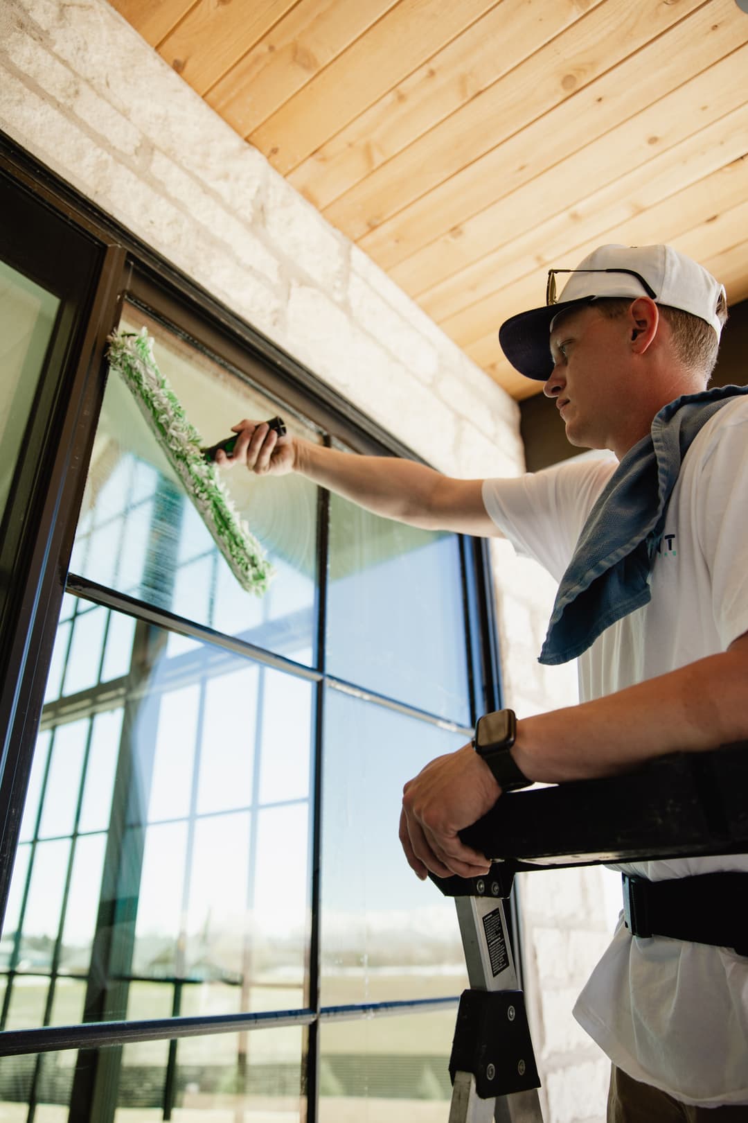 Window cleaning professional using a squeegee on large glass panes with a ladder.
