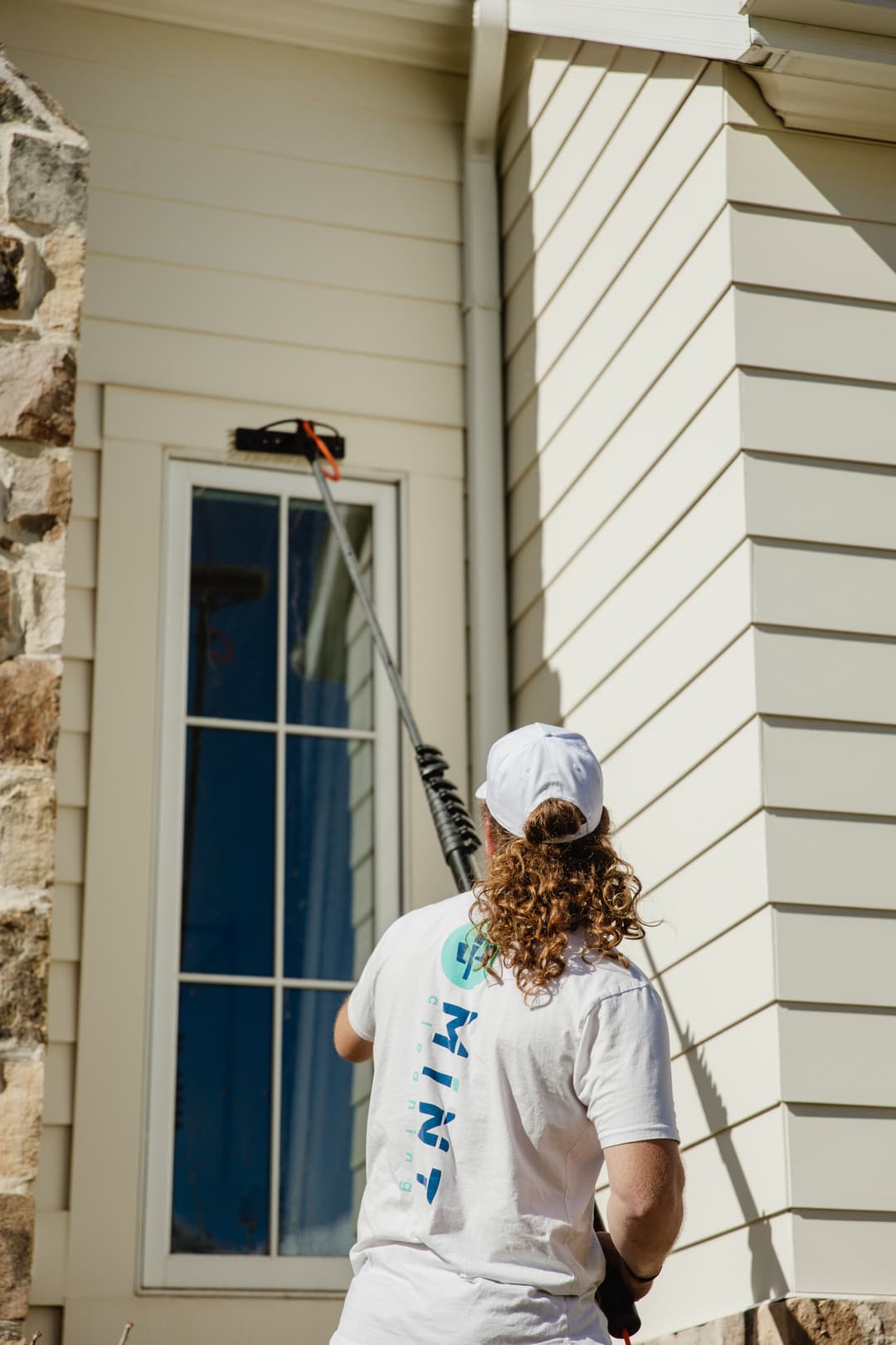 Person cleaning the exterior of a house with a long reach pole and brush.