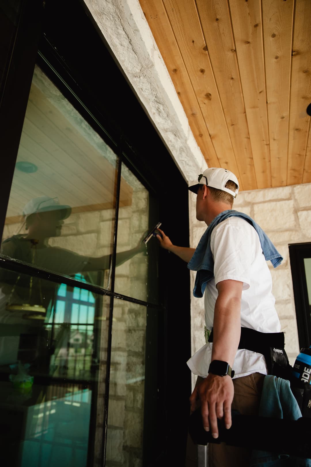 Person cleaning large glass windows in a modern home with a wooden ceiling.