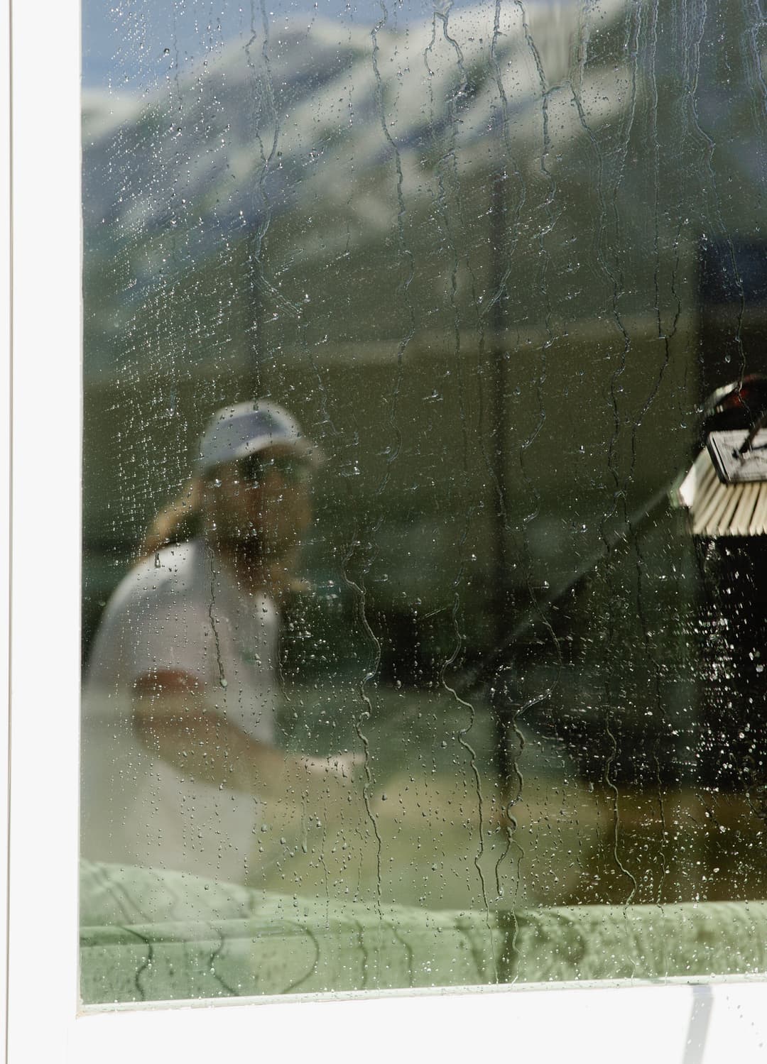 Window cleaner working outdoors, reflections and water droplets visible on the glass.