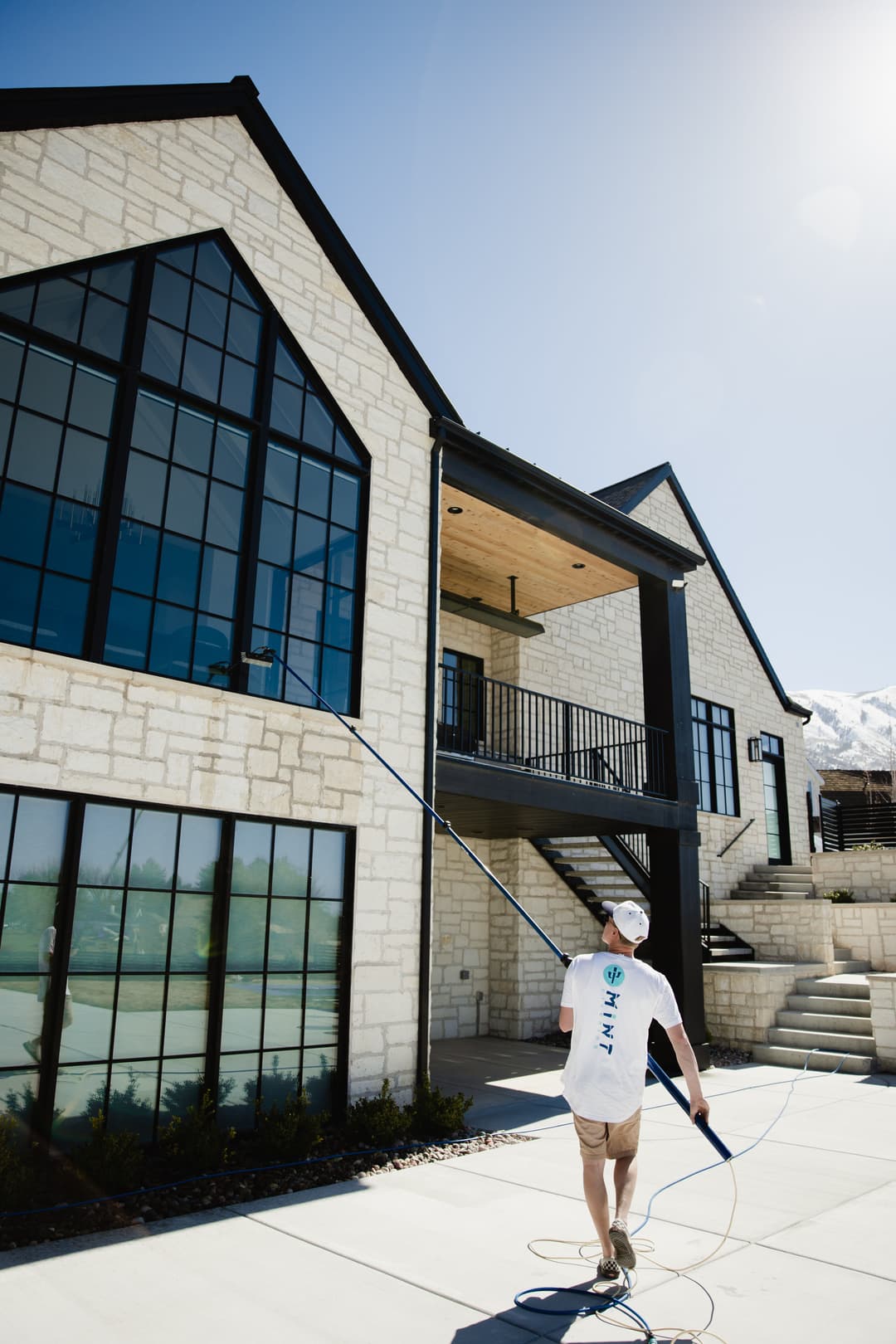Person painting the exterior of a modern home with large windows on a sunny day.