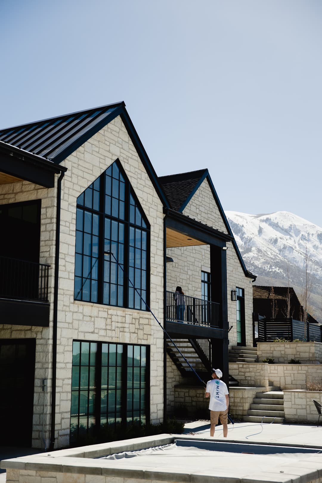 Home exterior with large windows, worker painting, and mountain backdrop on a clear day.