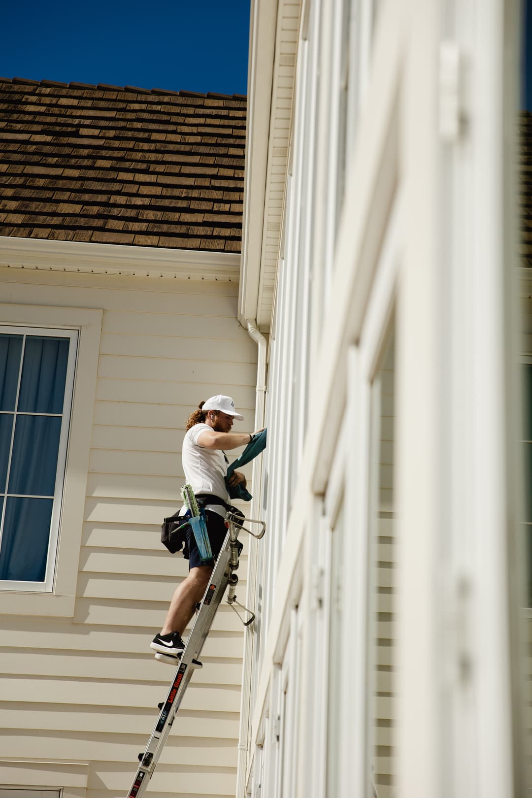 Man cleaning window from a ladder on a residential building. Bright sunny day.