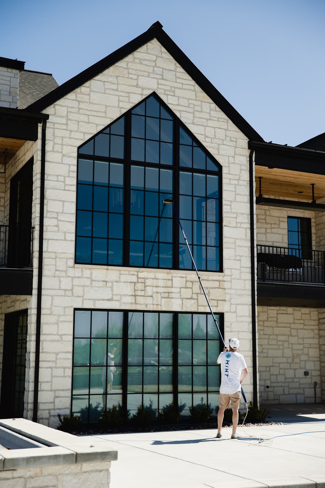 Worker cleaning large windows on a modern stone building under a clear blue sky.