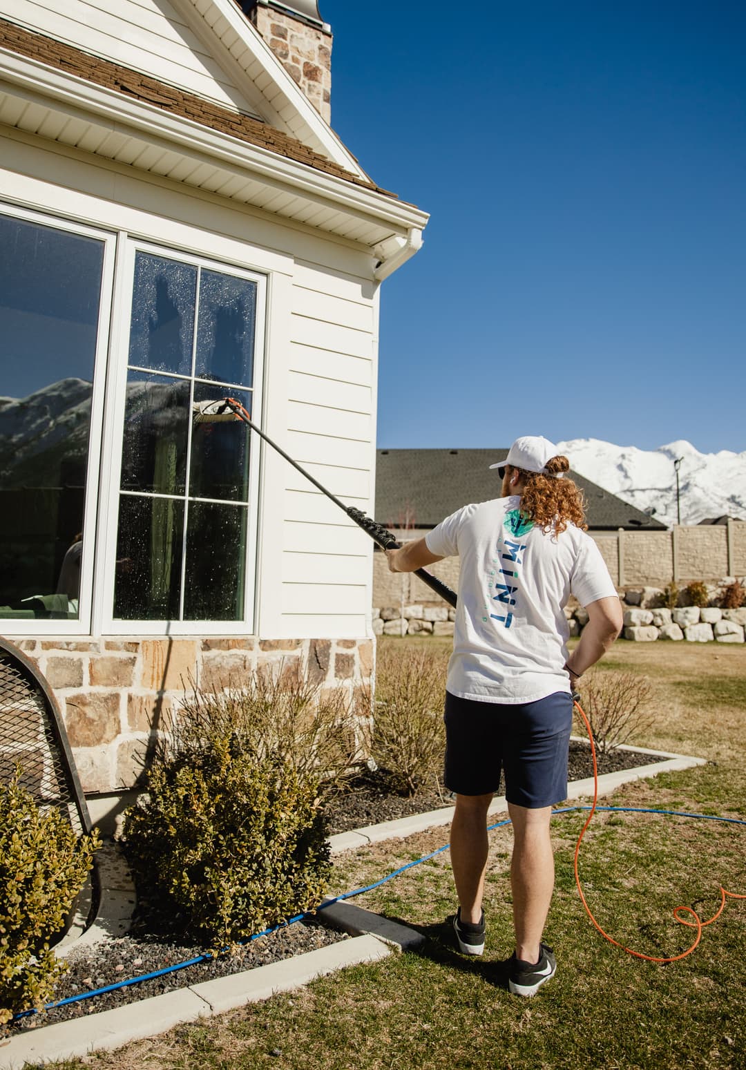 Person cleaning windows with a pressure washer on a sunny day outside a house.