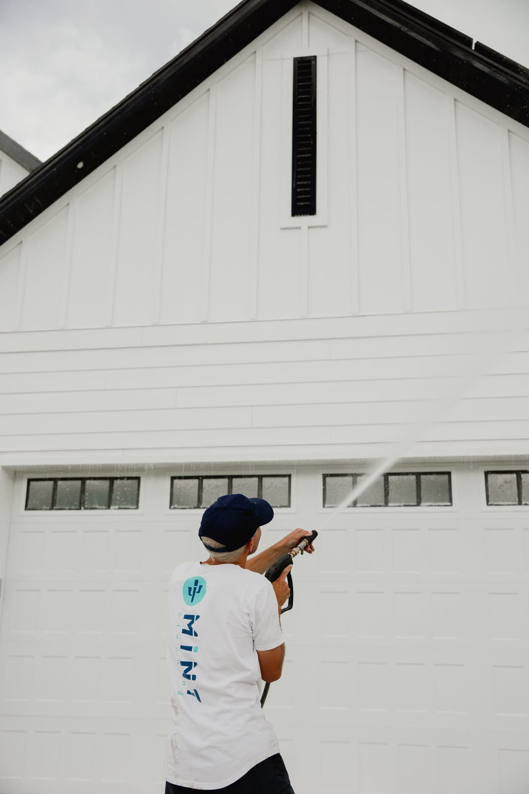 Person using a pressure washer on a white garage door of a house.