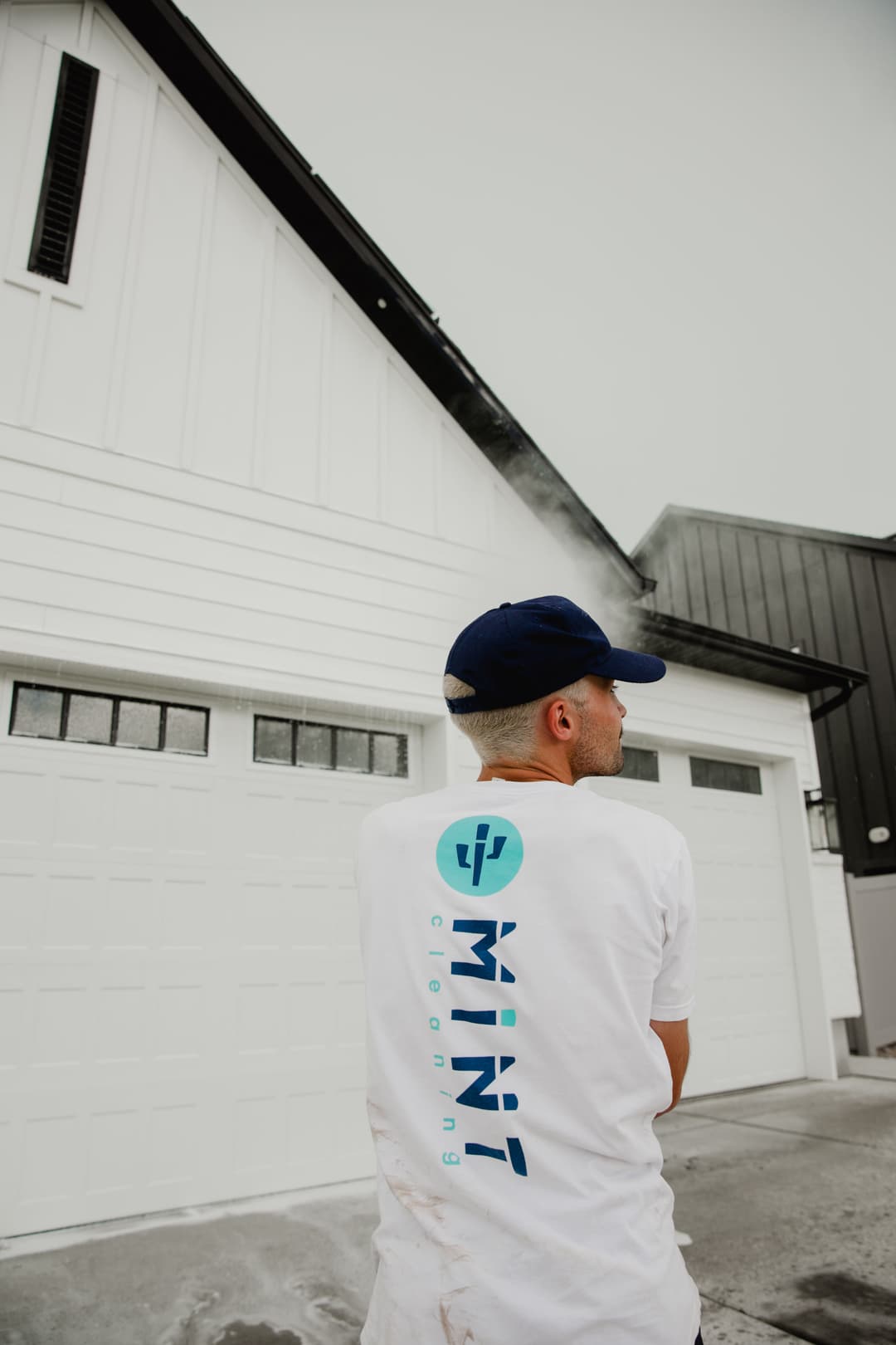 Man in a branded T-shirt stands by a modern garage, promoting Mint Cleaning services.