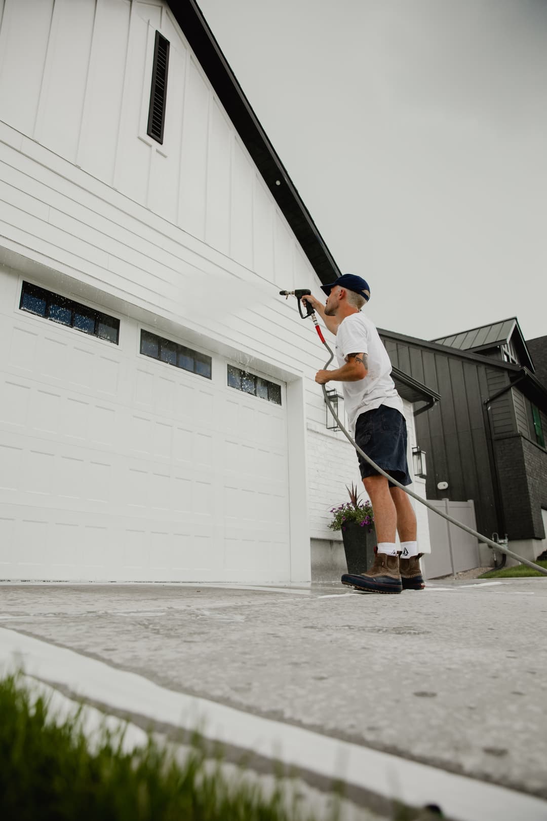 Person painting the exterior of a house with a spray gun on a cloudy day.