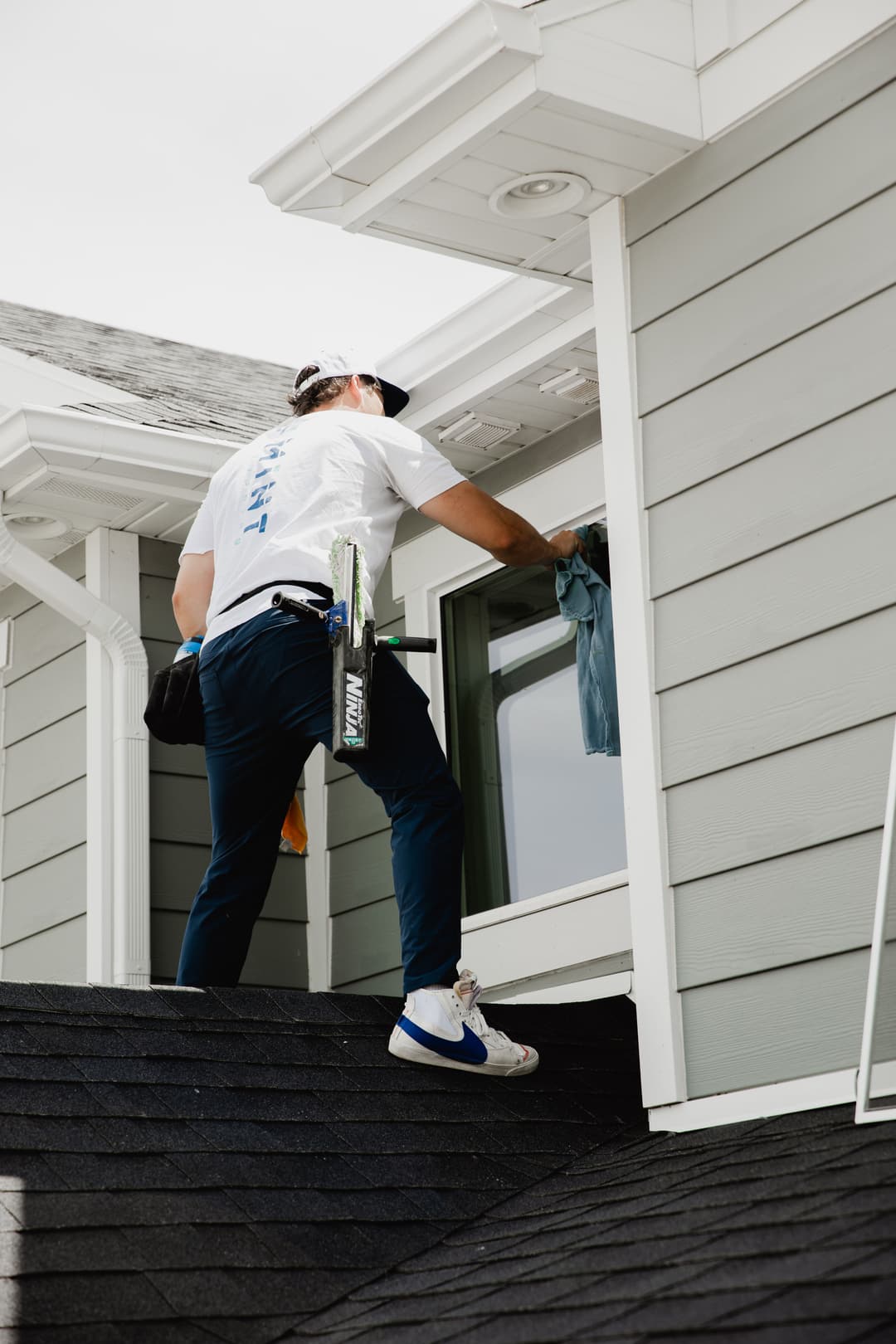 Window cleaning professional working on a residential roof, using tools and a cloth.