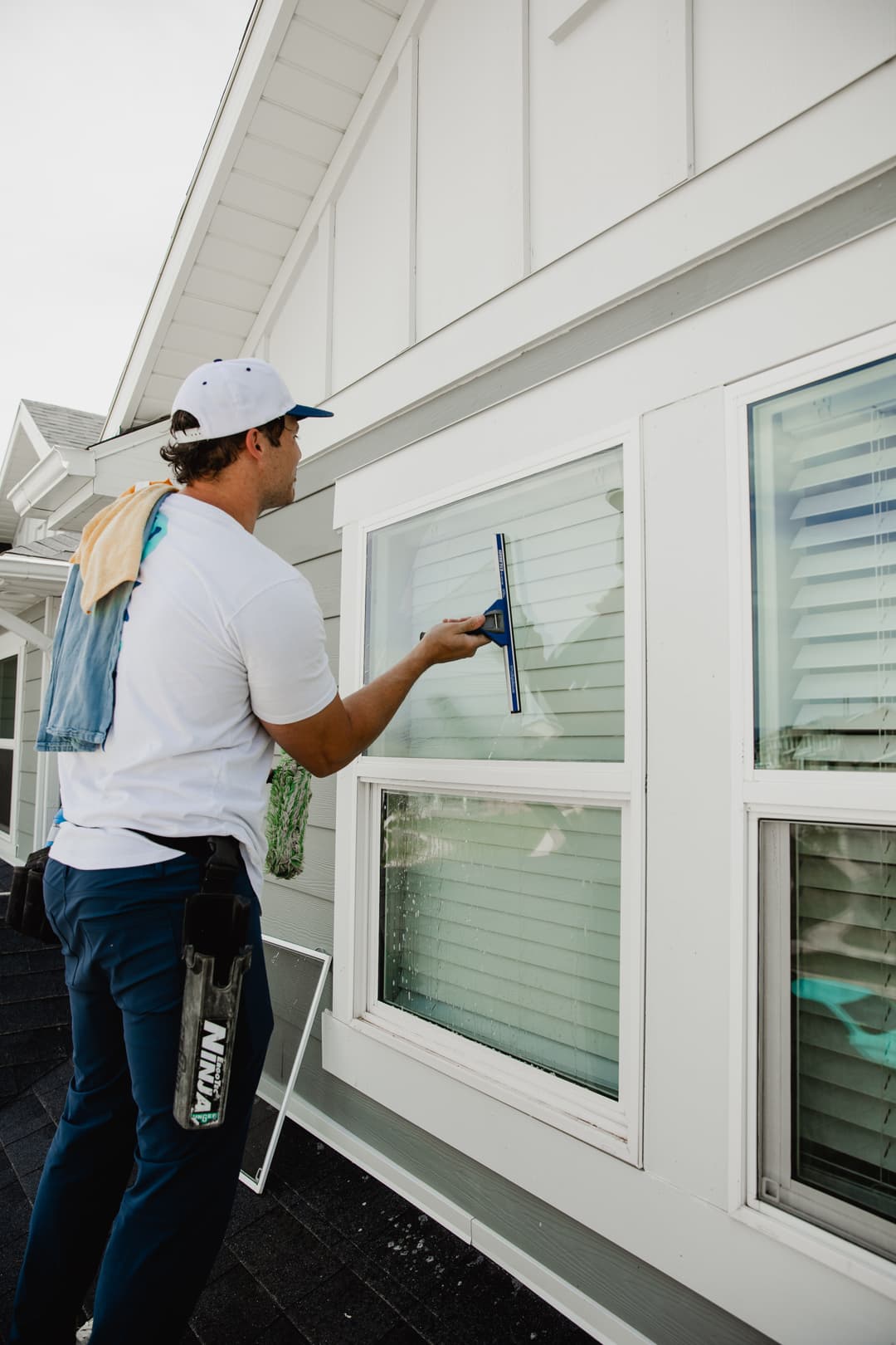 Window cleaner in a white cap using a squeegee on a house's exterior windows.