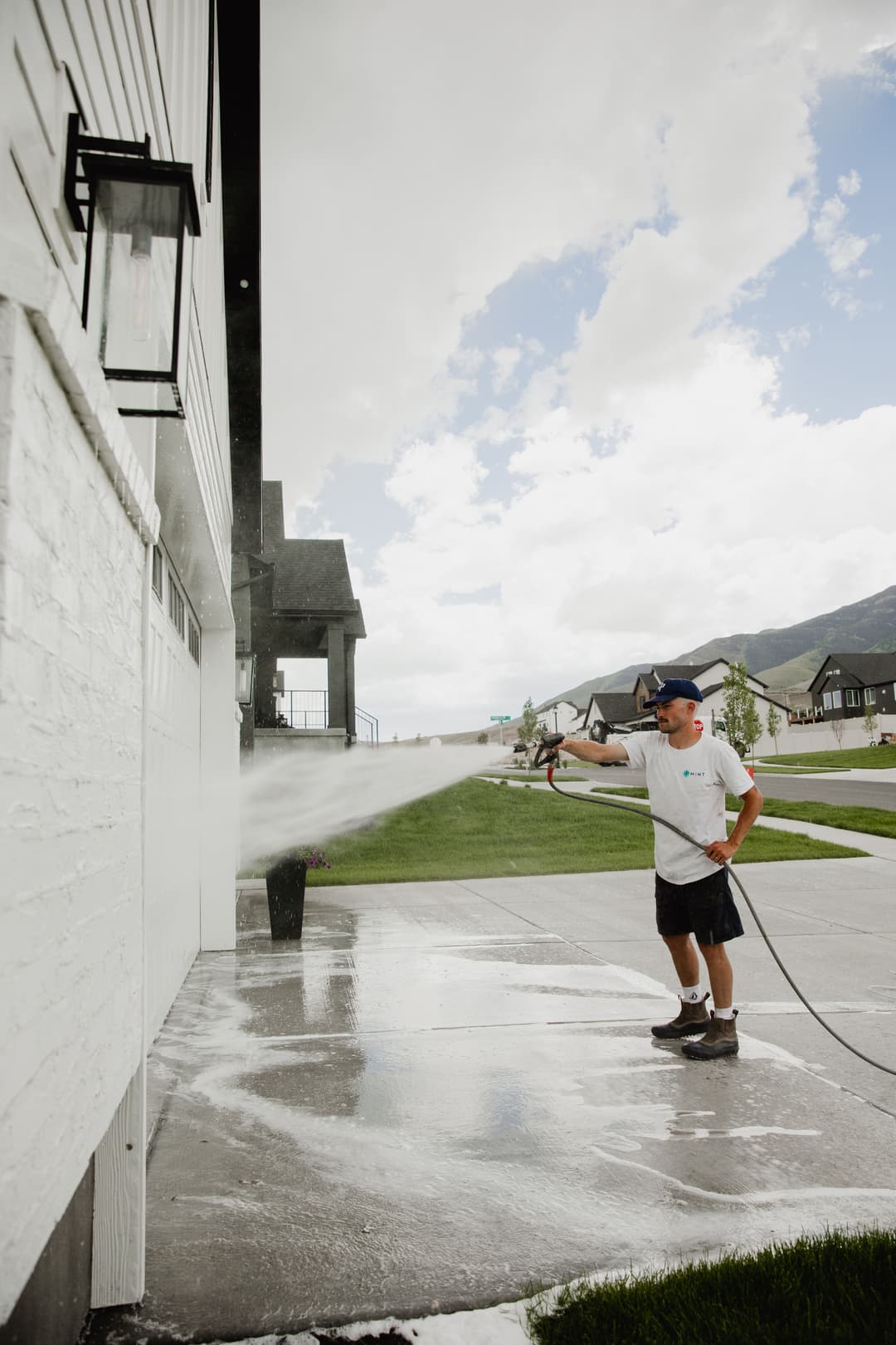 Homeowner using a pressure washer to clean exterior walls on a sunny day.