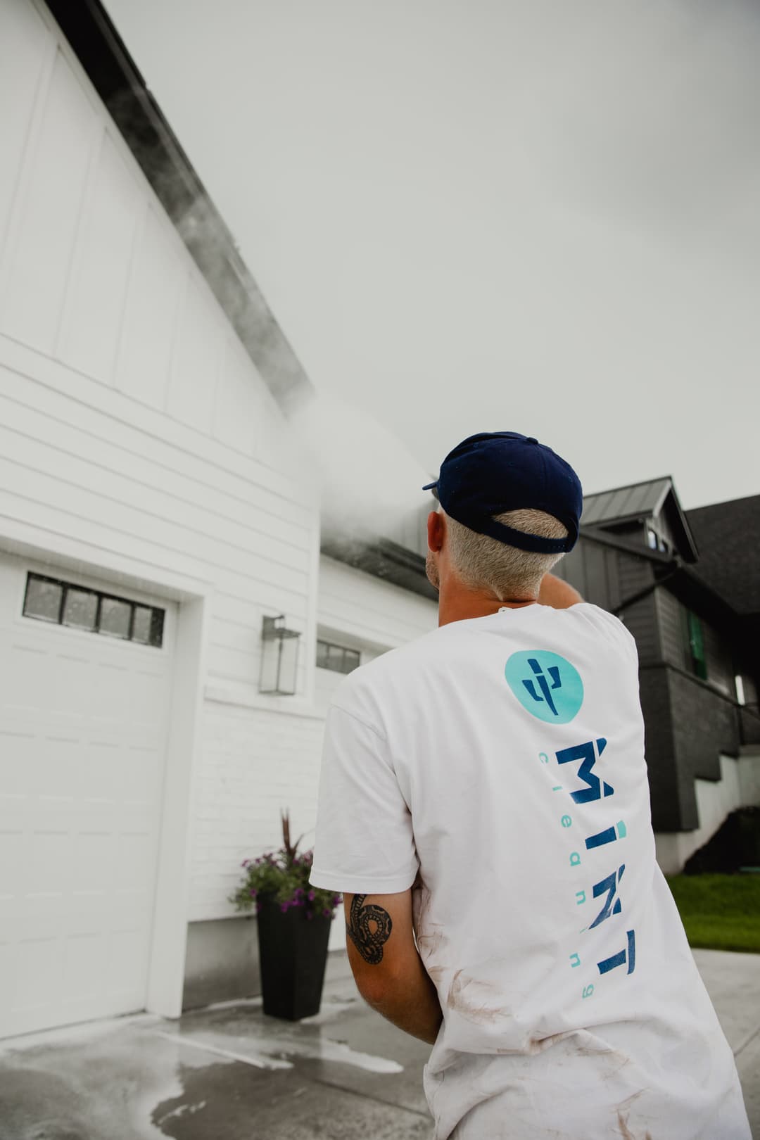 Pressure washing a home's exterior by Mint Cleaning professional in a gray sky.