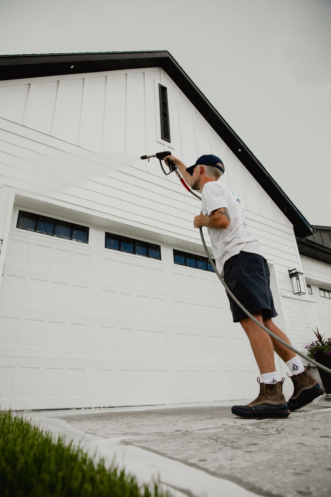 Man using a paint sprayer to refresh the exterior of a white house with a garage.