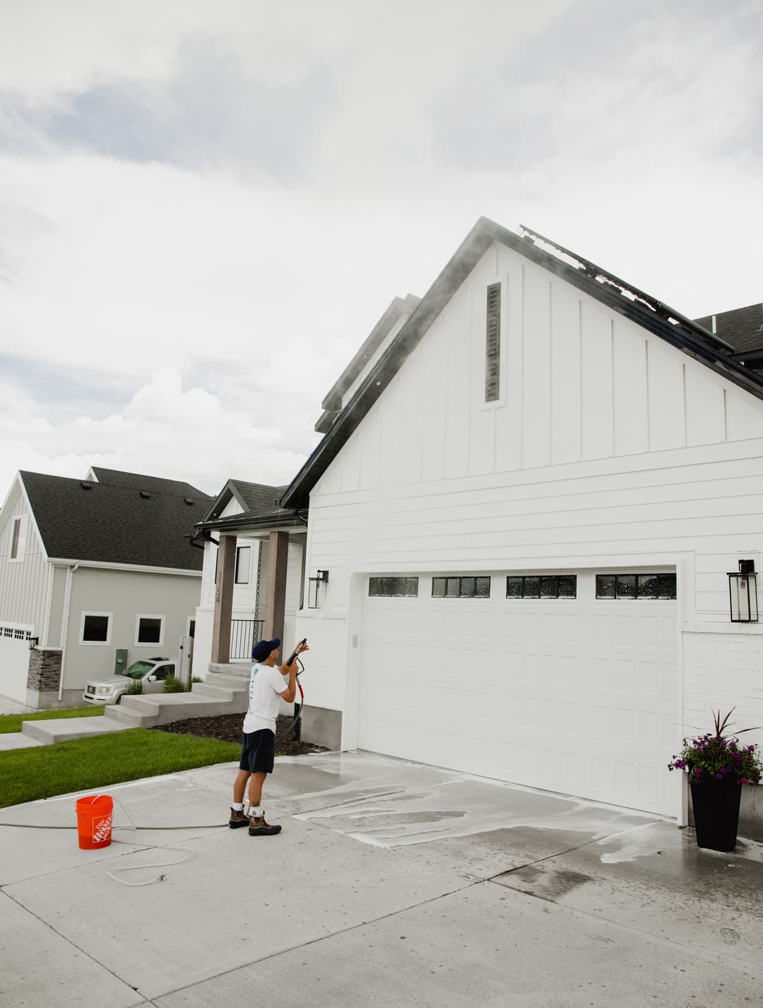 Person using a pressure washer to clean the exterior of a modern white house.