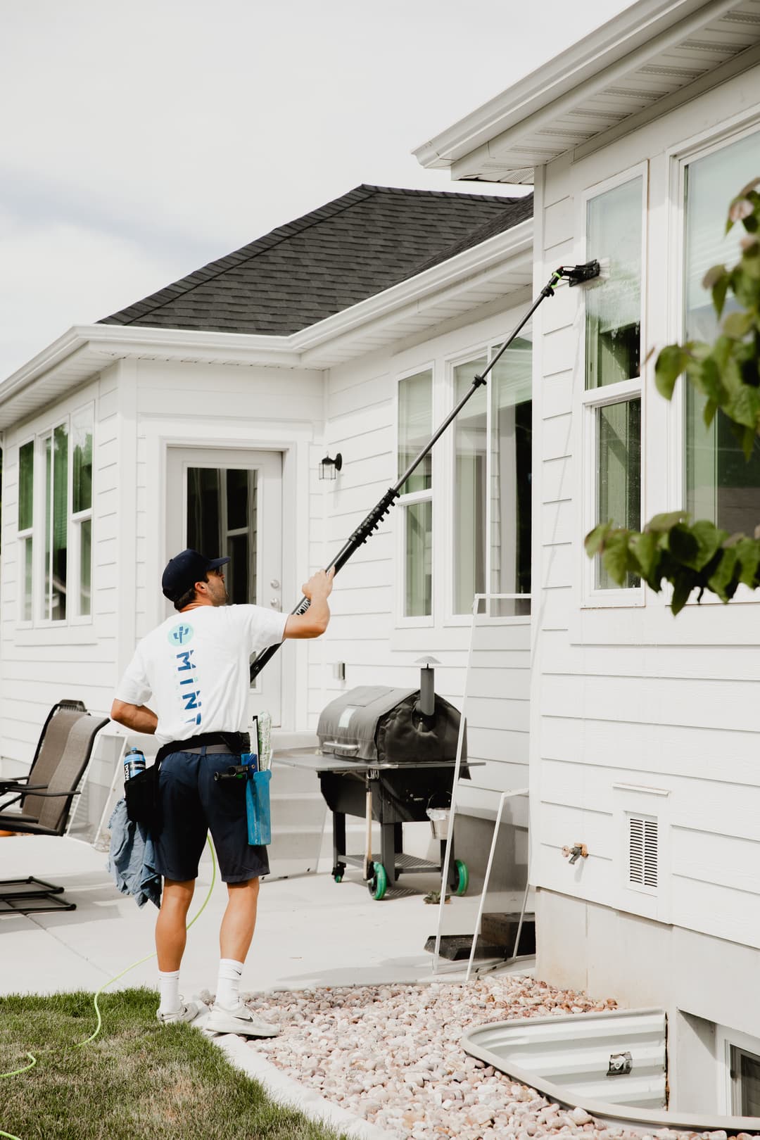 Professional window cleaner using a pole to wash exterior windows of a residential home.