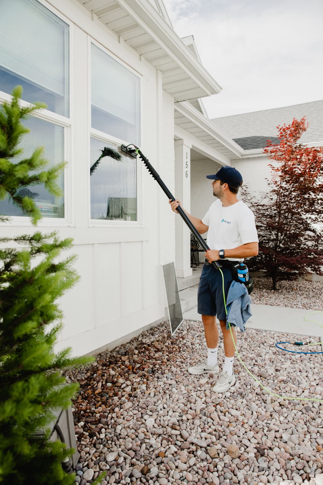 Professional window cleaner using a pole to wash windows on a residential home exterior.