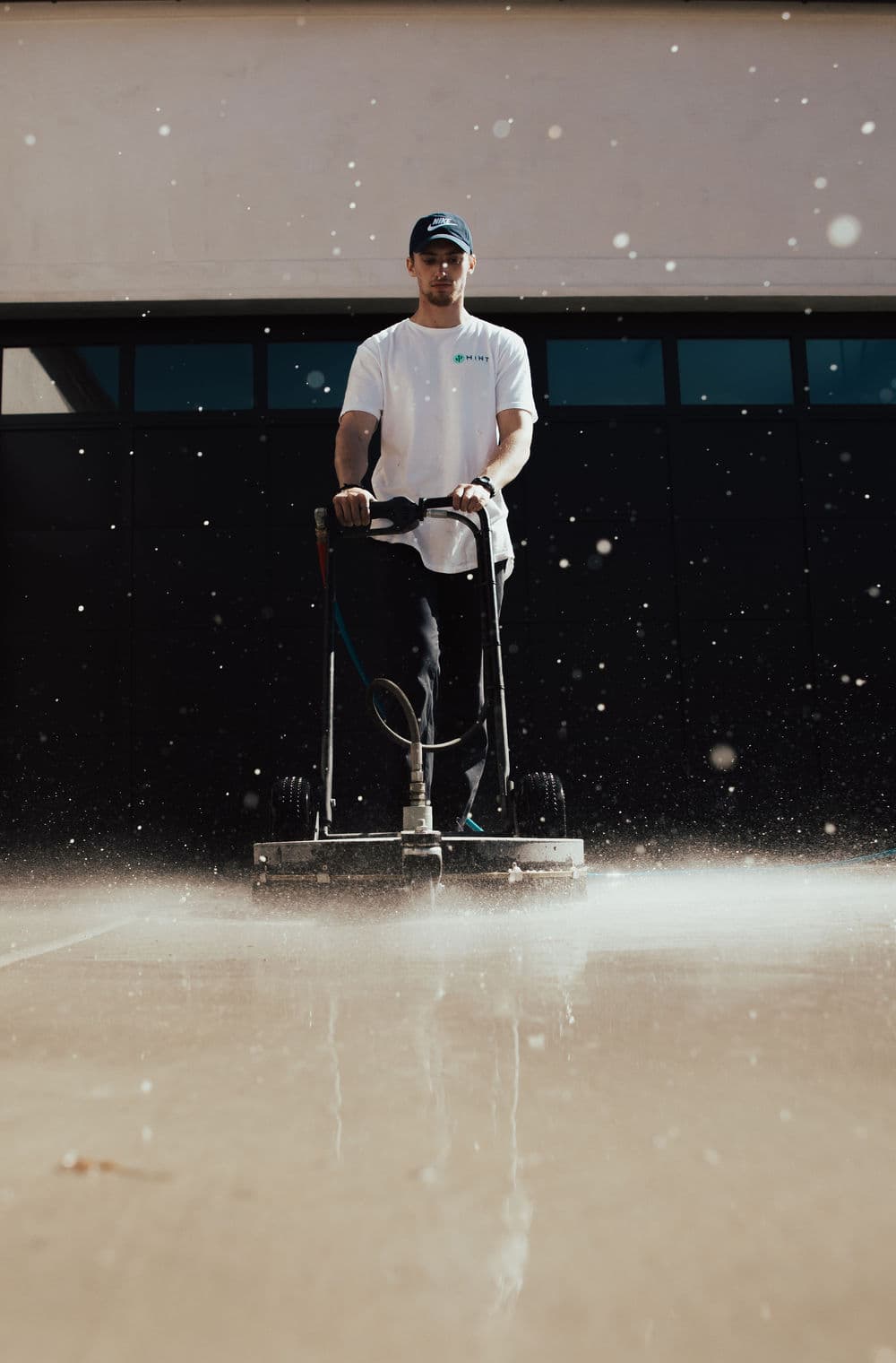 Person using a concrete grinder on a smooth surface, water spray and droplets visible.