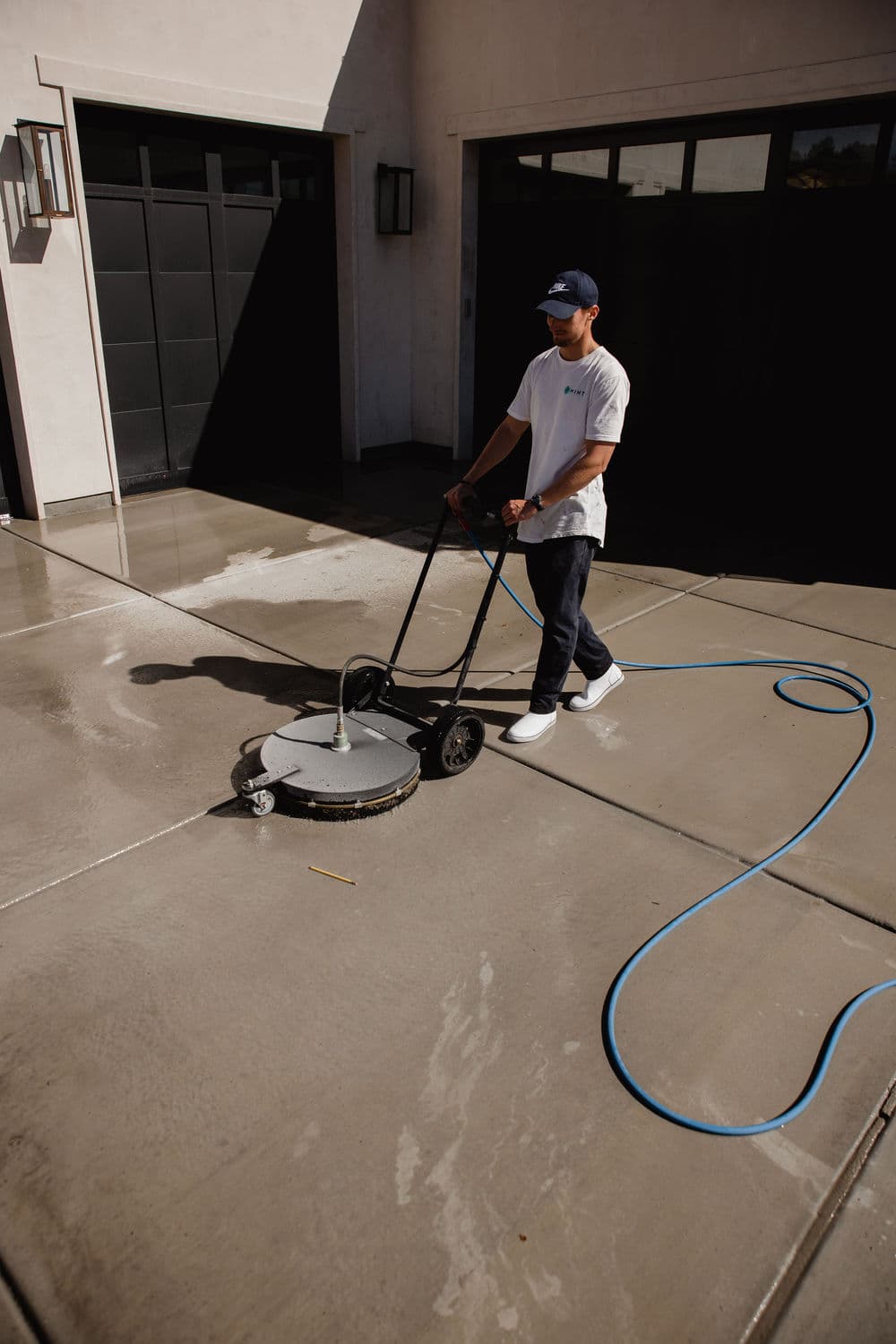 Person using a surface cleaner to wash a concrete driveway outside a modern home.