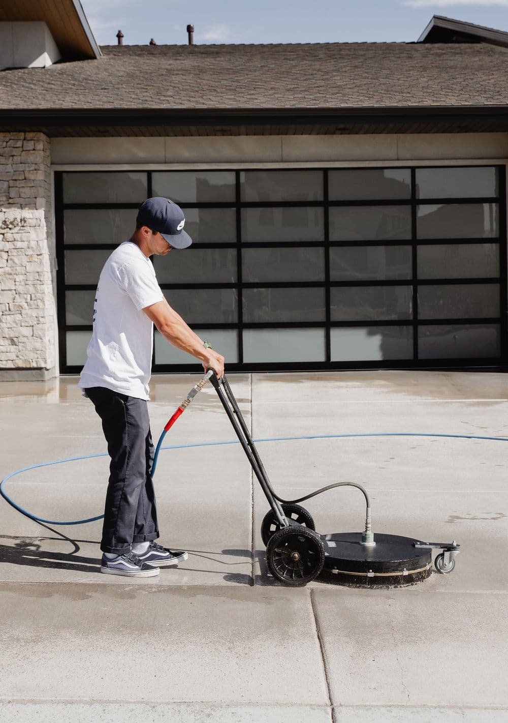 Person using a pressure washer on a concrete surface outside a modern building.