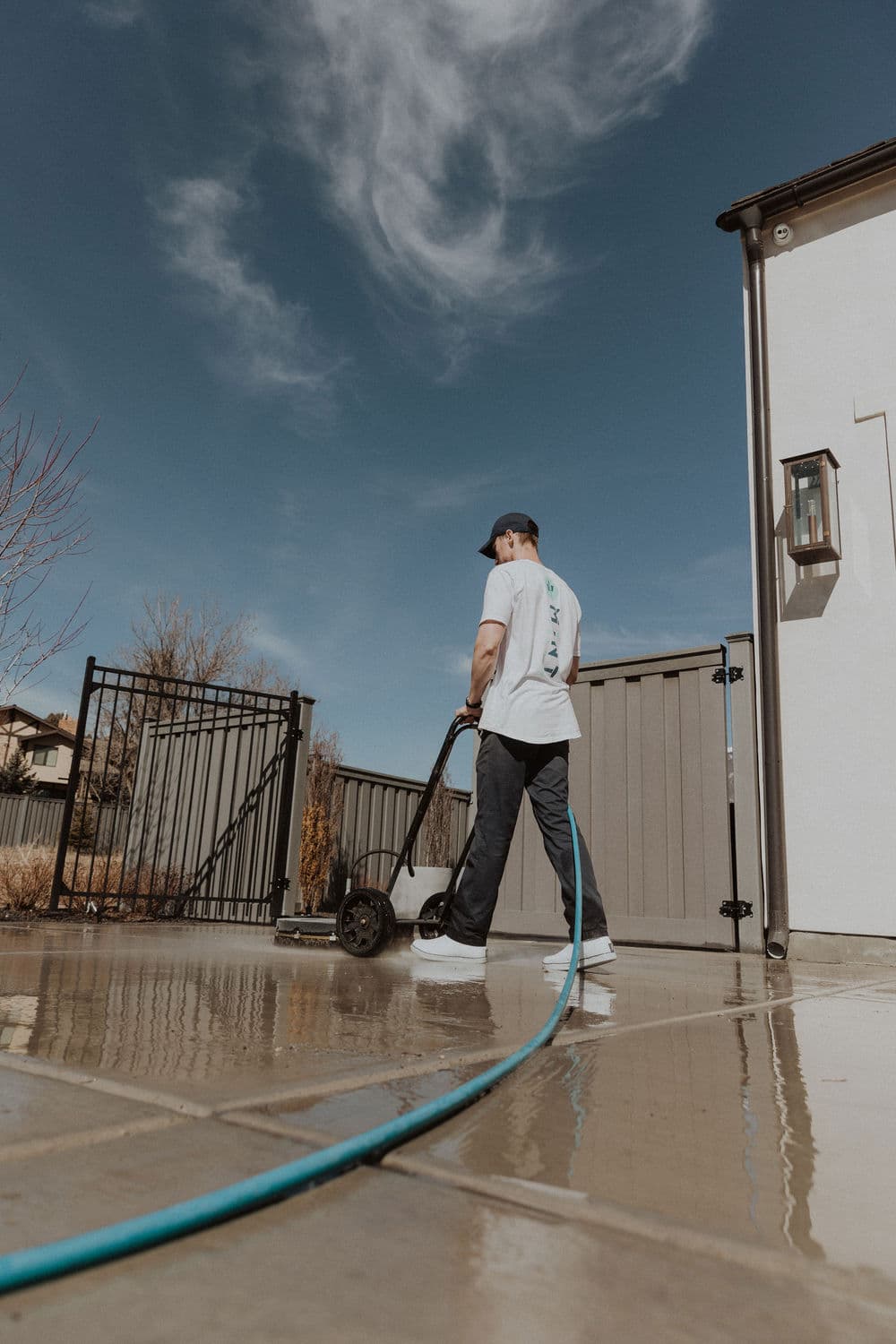 Person pressure washing a patio with water hose under a clear blue sky.