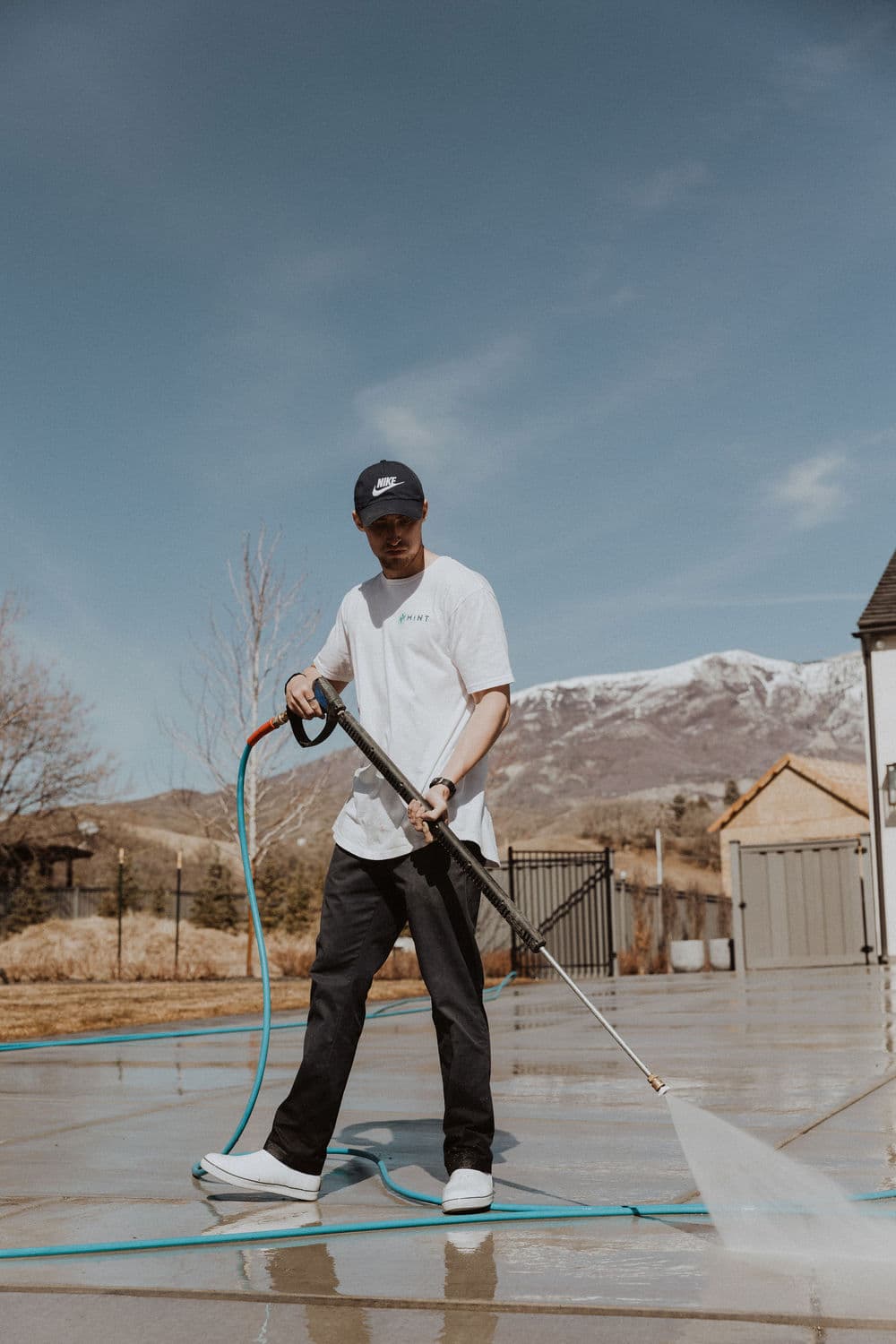 Man using a pressure washer on a patio with mountains in the background under a clear sky.