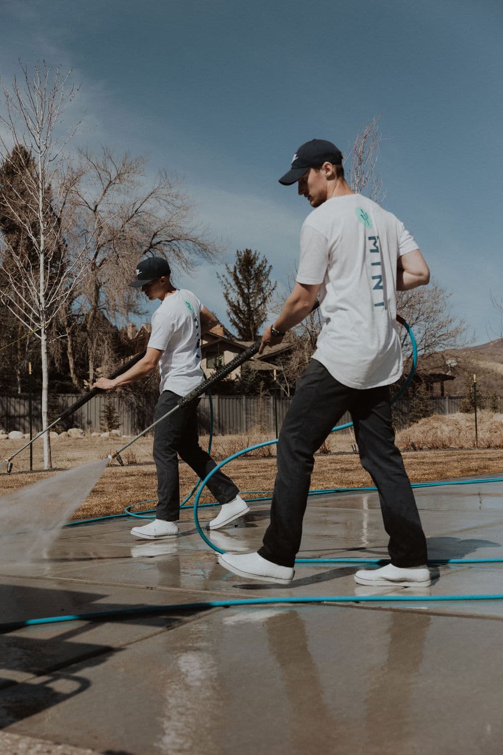 Two workers pressure washing a patio outdoors on a sunny day.