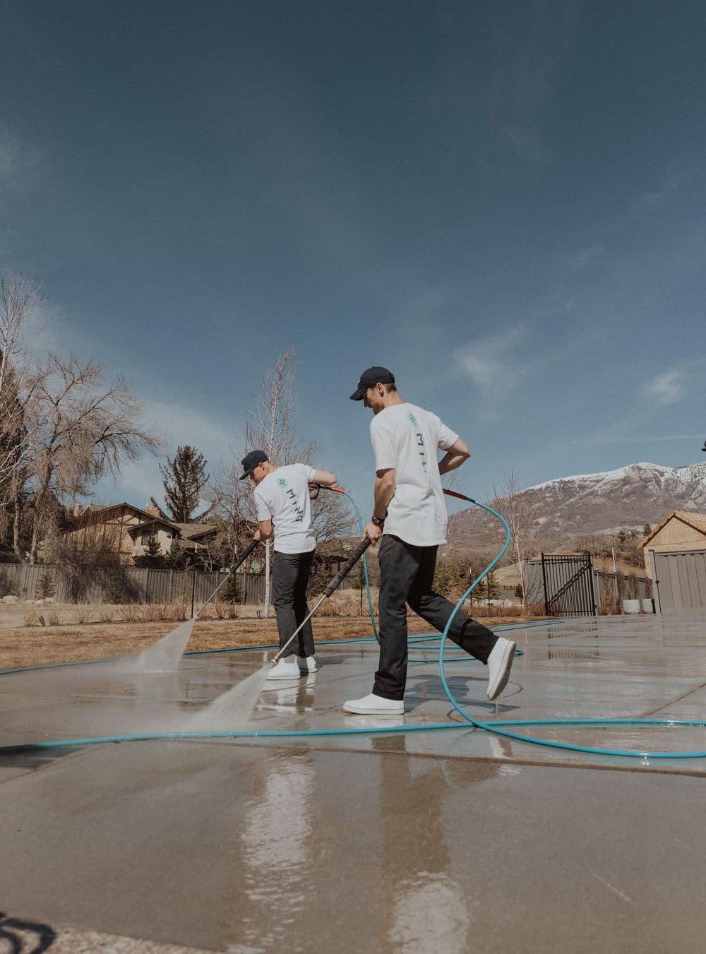 Two workers power washing a concrete surface with hoses in a residential area.