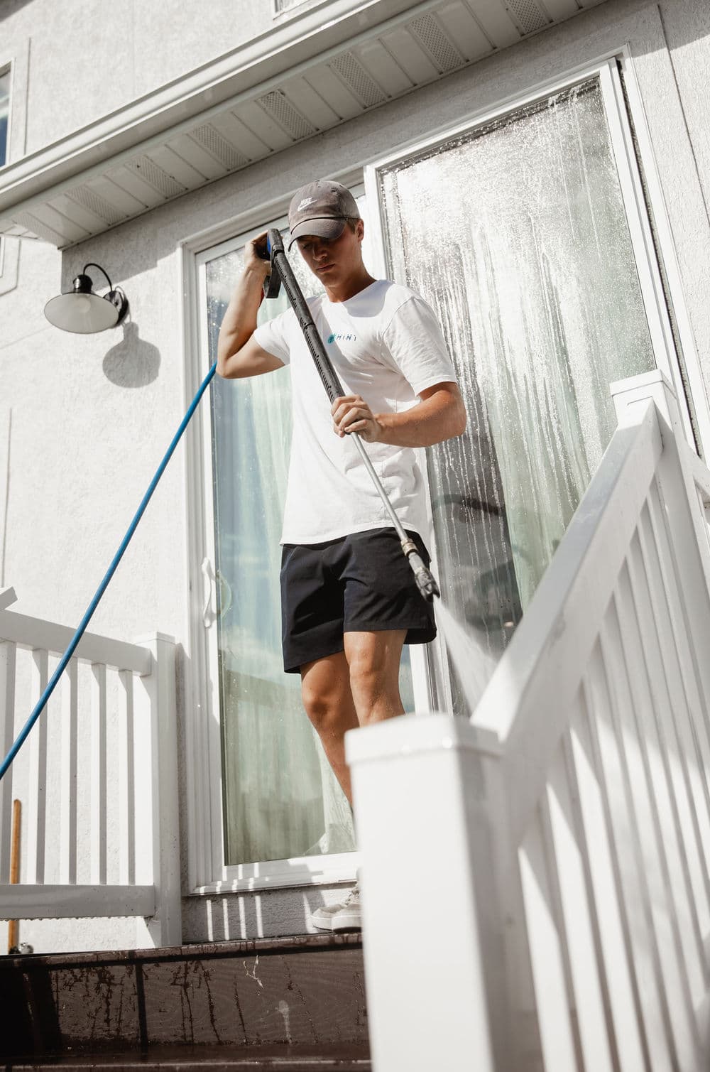 Man cleaning a porch with a power washer on a sunny day, wearing casual attire.