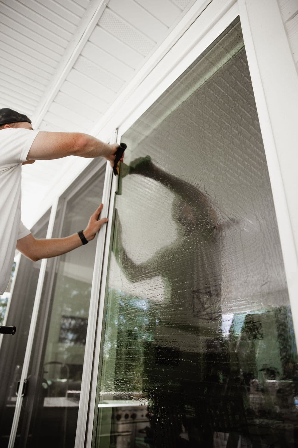 Person installing a screen door with a focus on their reflection on the glass surface.