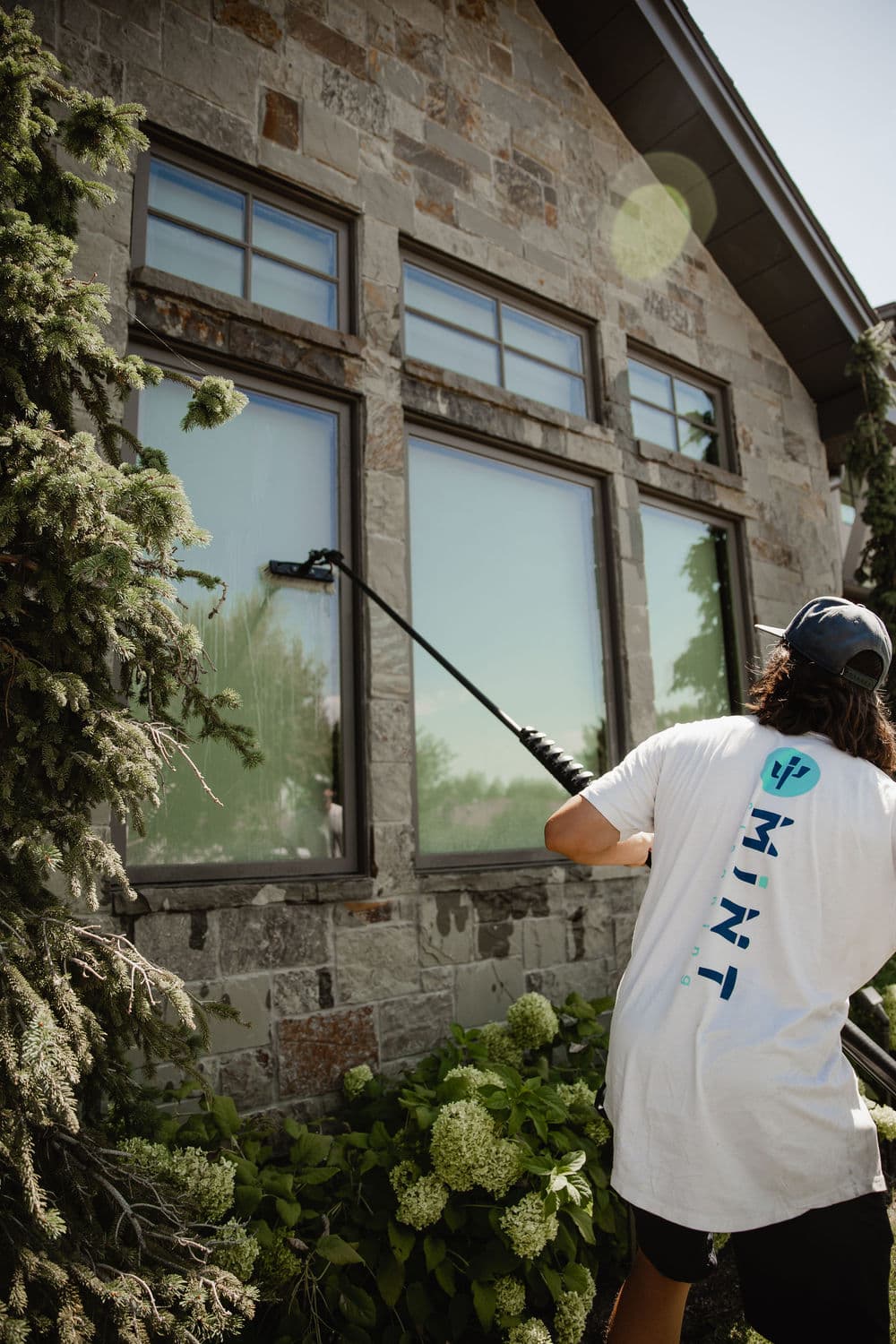 Window cleaning service in action with professional using extension pole on large stone house.