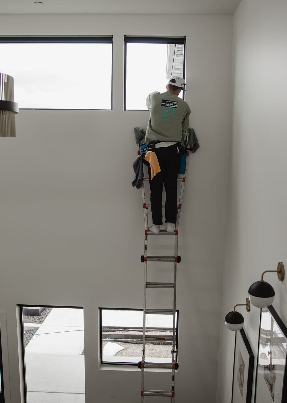 Person on a ladder cleaning a high window in a modern home interior.