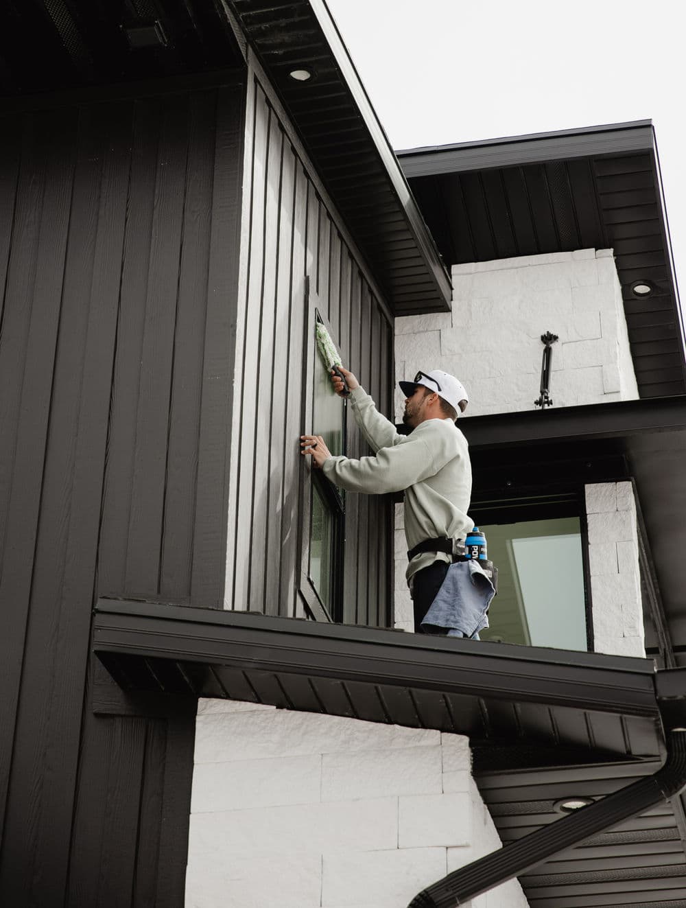Contractor painting exterior of modern house with black siding and white stone accents.