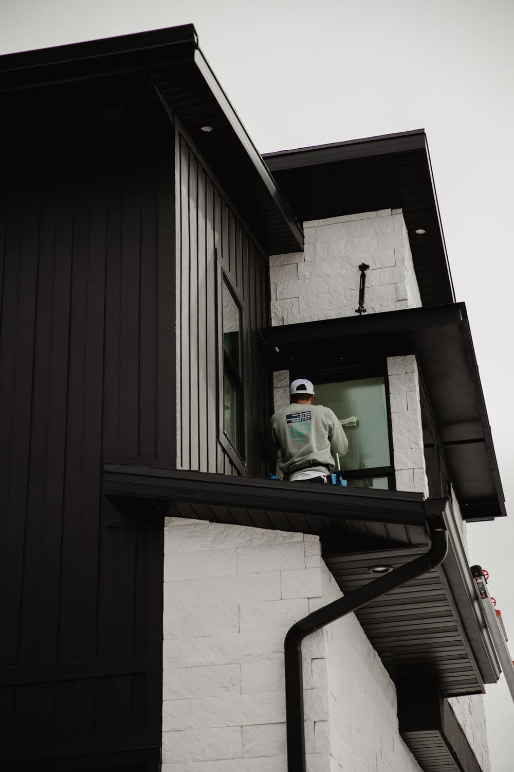 Worker painting exterior of modern two-story house with black wood and white stone accents.