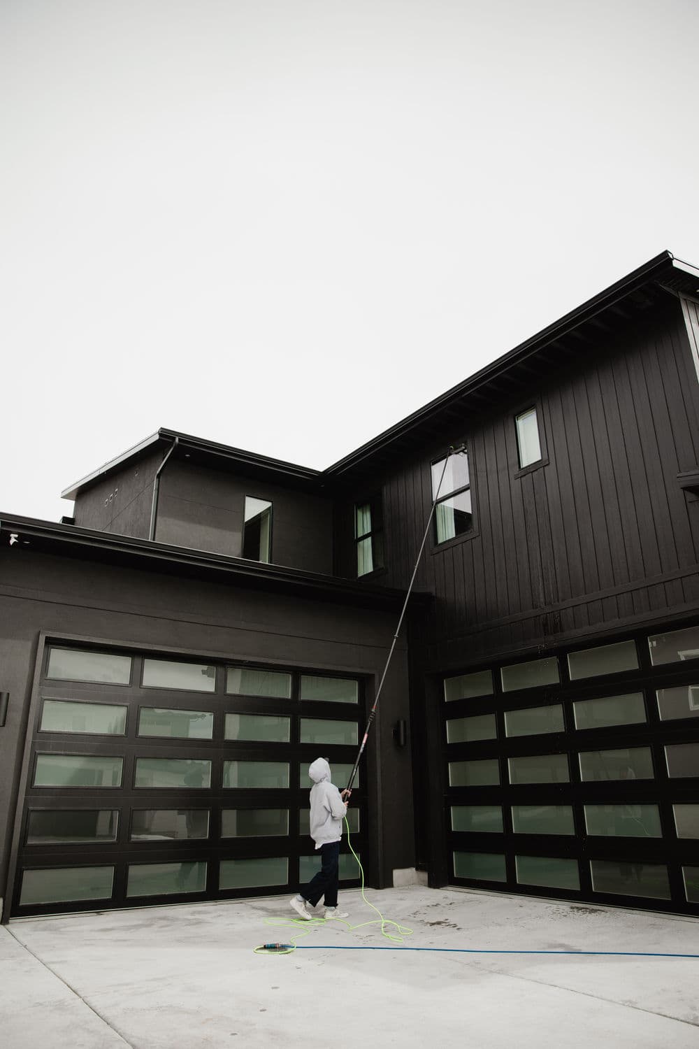 Person using a pole to clean the exterior of a modern black house with large windows.