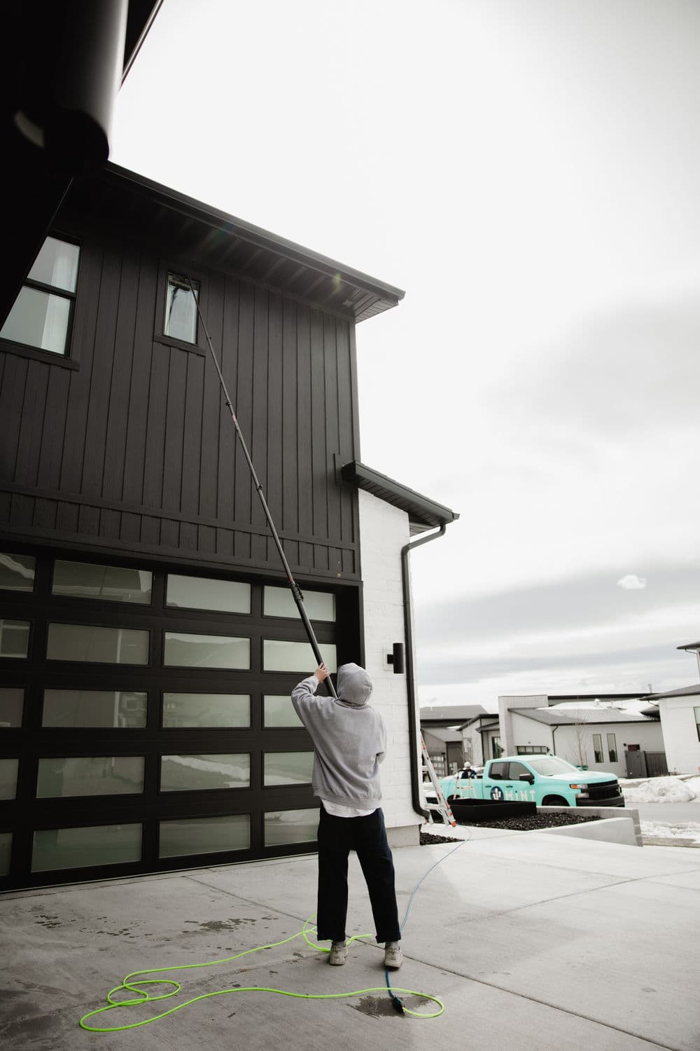Person using a pole to wash high windows on a modern black house exterior.