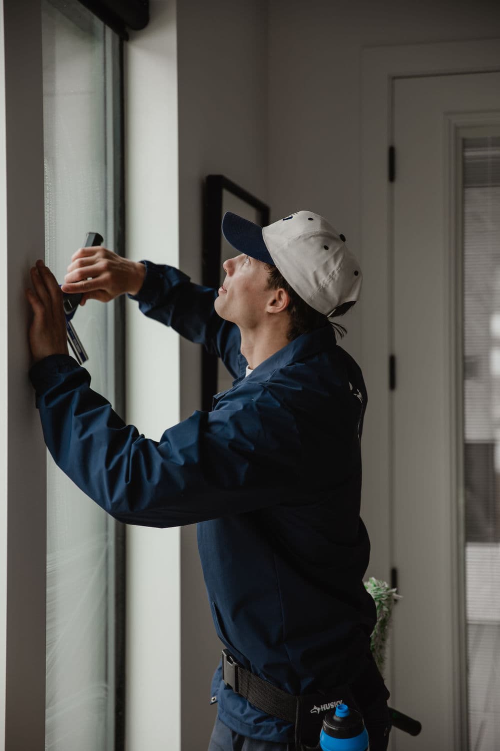 Person in blue jacket cleaning window with squeegee in modern indoor setting.