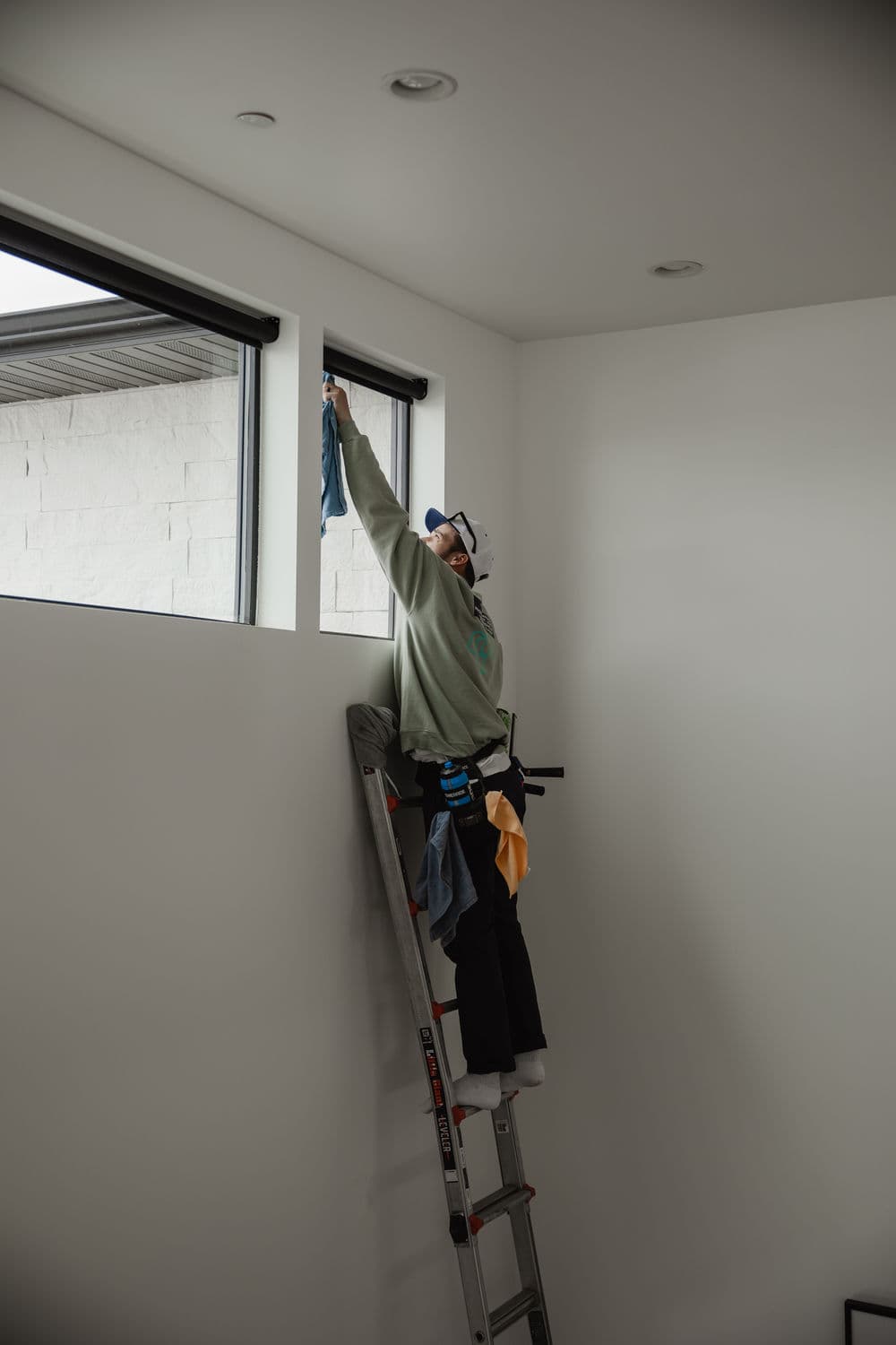 Person cleaning a high window on a ladder in a modern interior space.