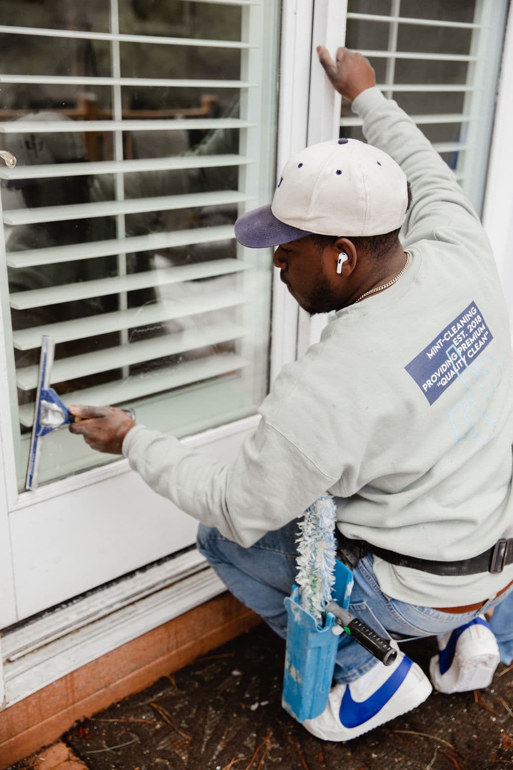 Man cleaning a window with a squeegee, wearing headphones and a gray sweatshirt.