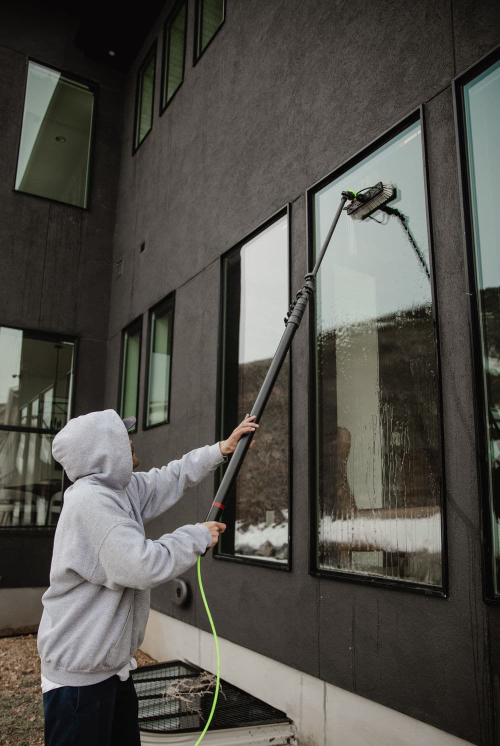 Person using a long pole to clean large windows on a modern building exterior.