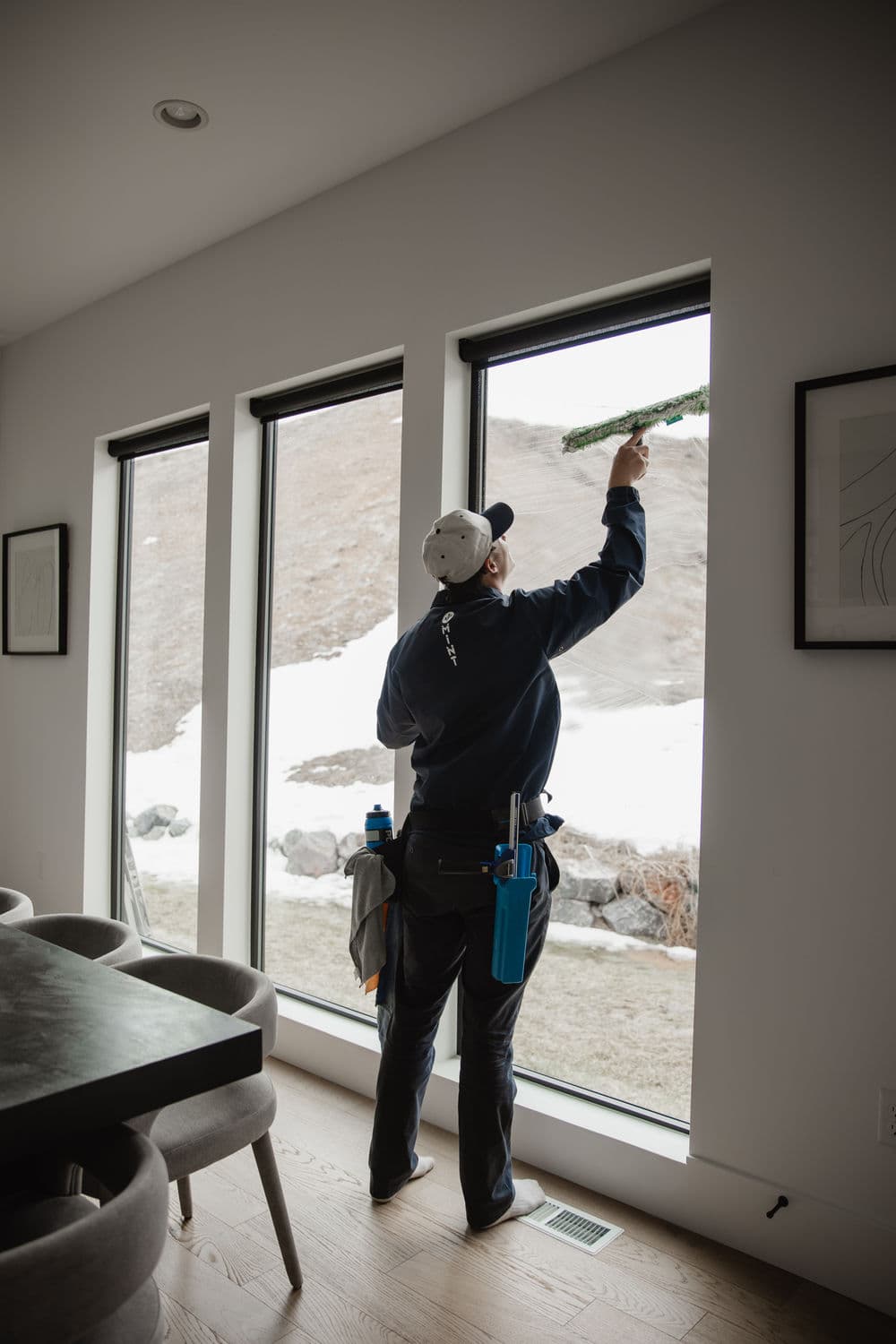 Window cleaner using a squeegee on large, modern windows in a bright interior space.