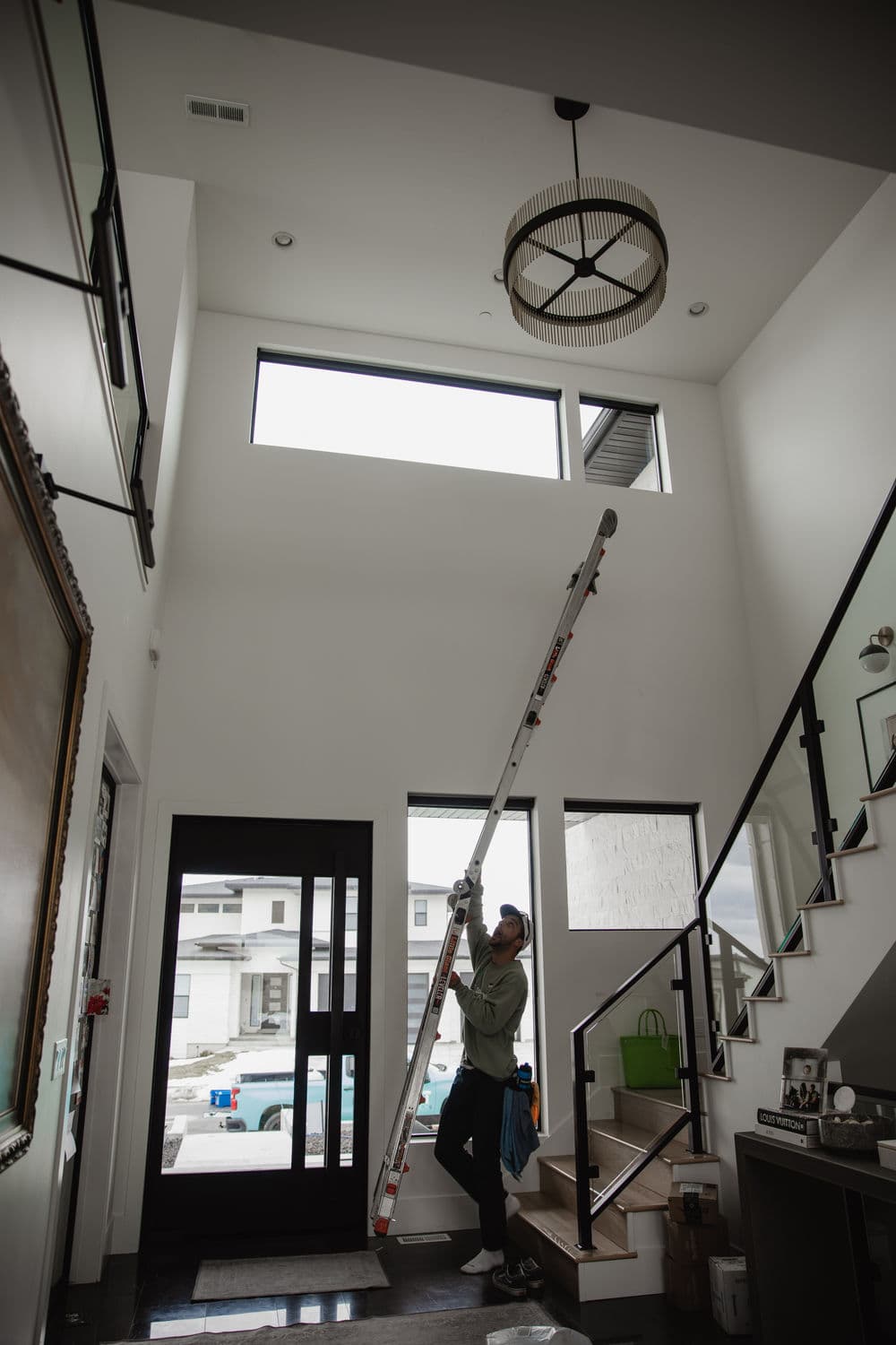 Person using a ladder to adjust a light fixture in a modern home entryway with tall ceilings.