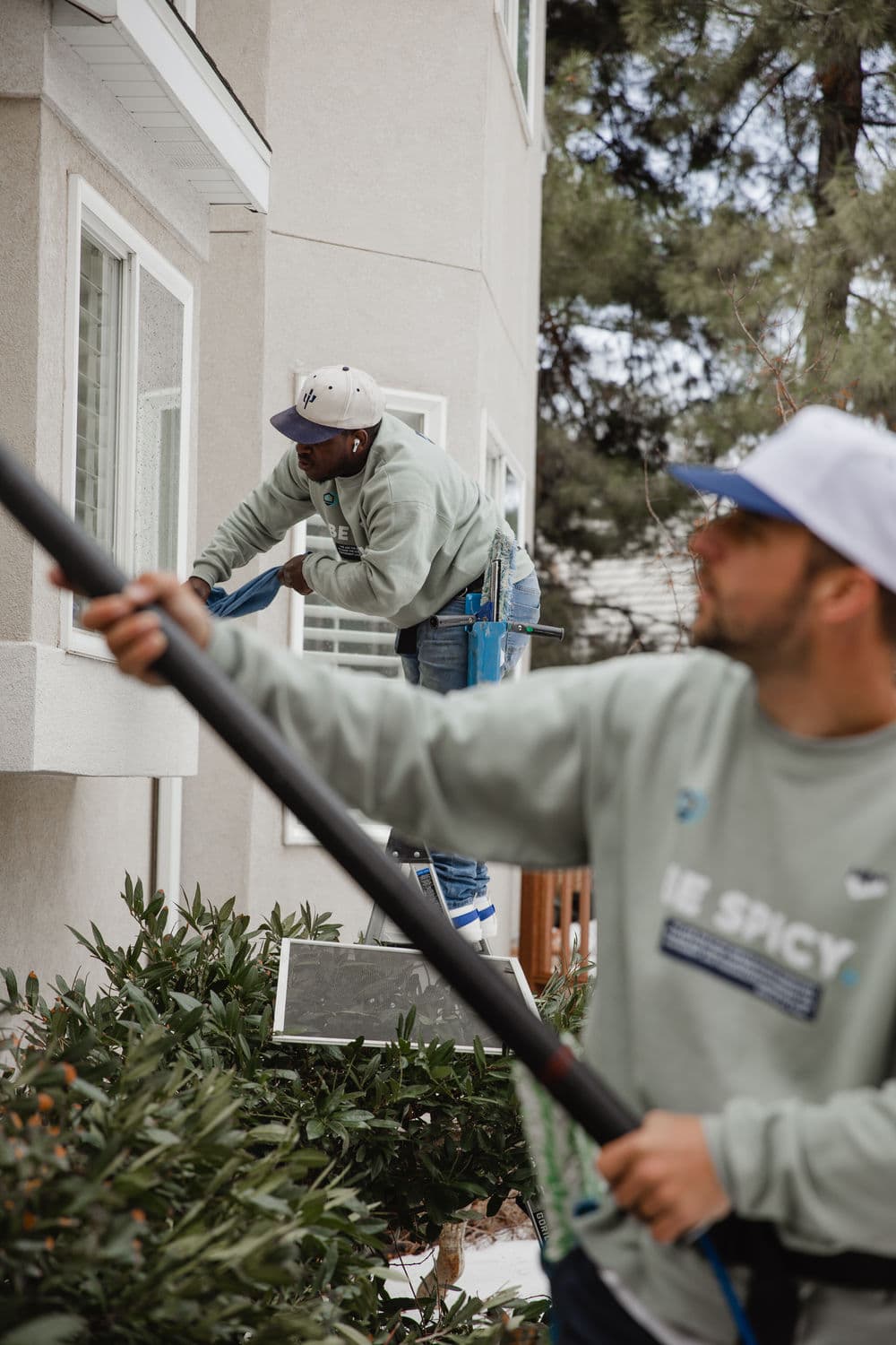 Two window cleaners in gray sweatshirts working on a building exterior.