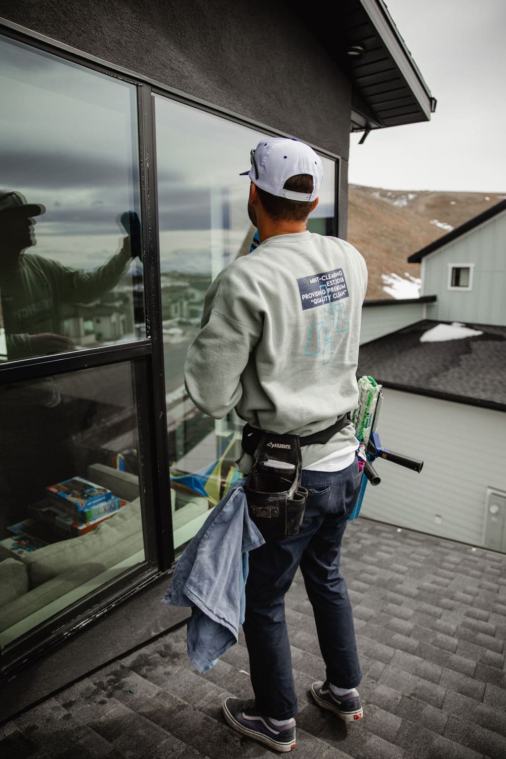 Window cleaner using a squeegee on a modern home with a scenic backdrop.
