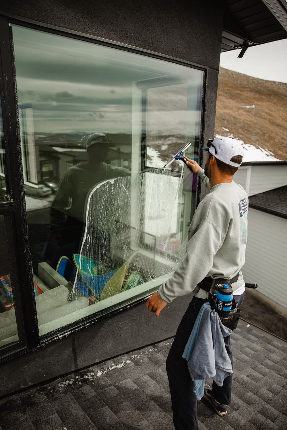 Professional window cleaner using squeegee on large residential glass window.