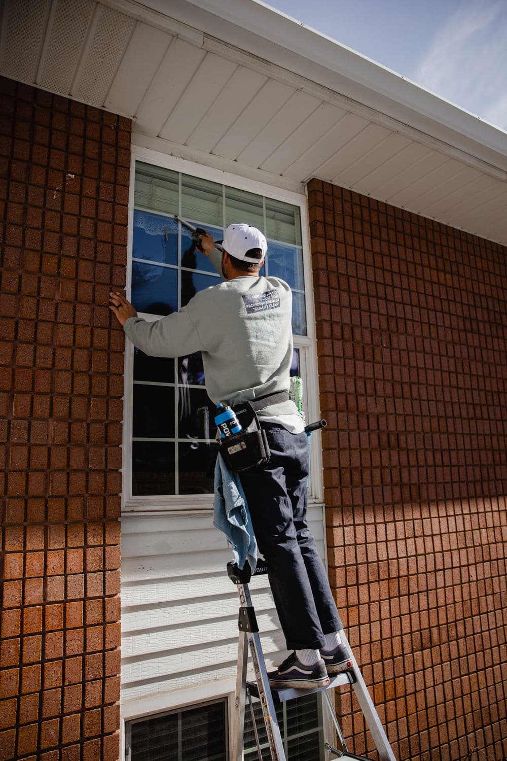Worker cleaning window from ladder on brick building exterior.