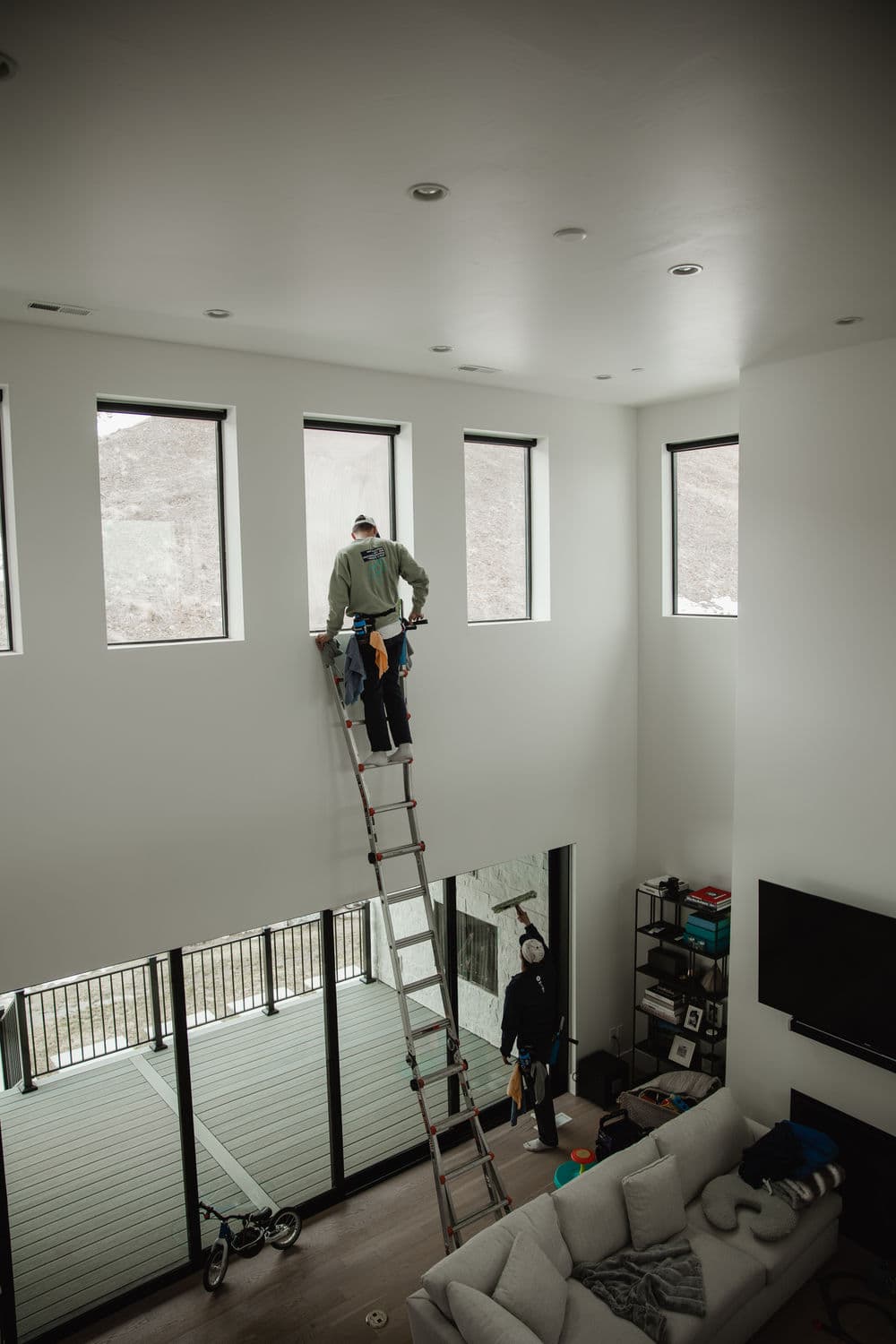 Two workers installing windows in a spacious, modern living room with a ladder.
