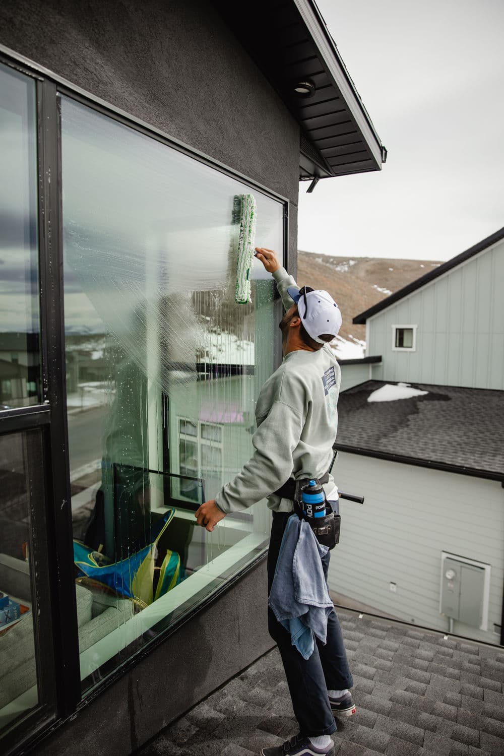 Man cleaning windows on a house rooftop with a squeegee and cleaning solution.